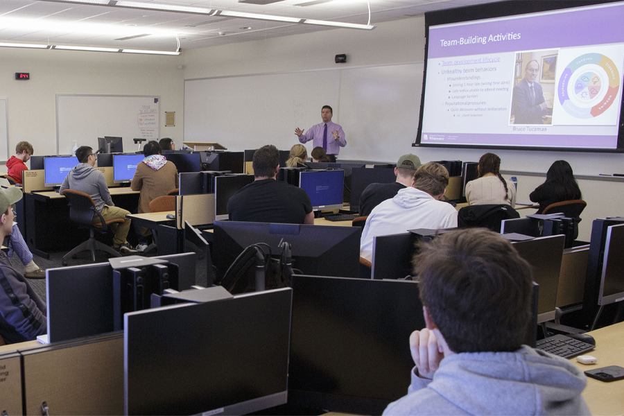 A group of international business students speak to a group in an auditorium with purple lighting.